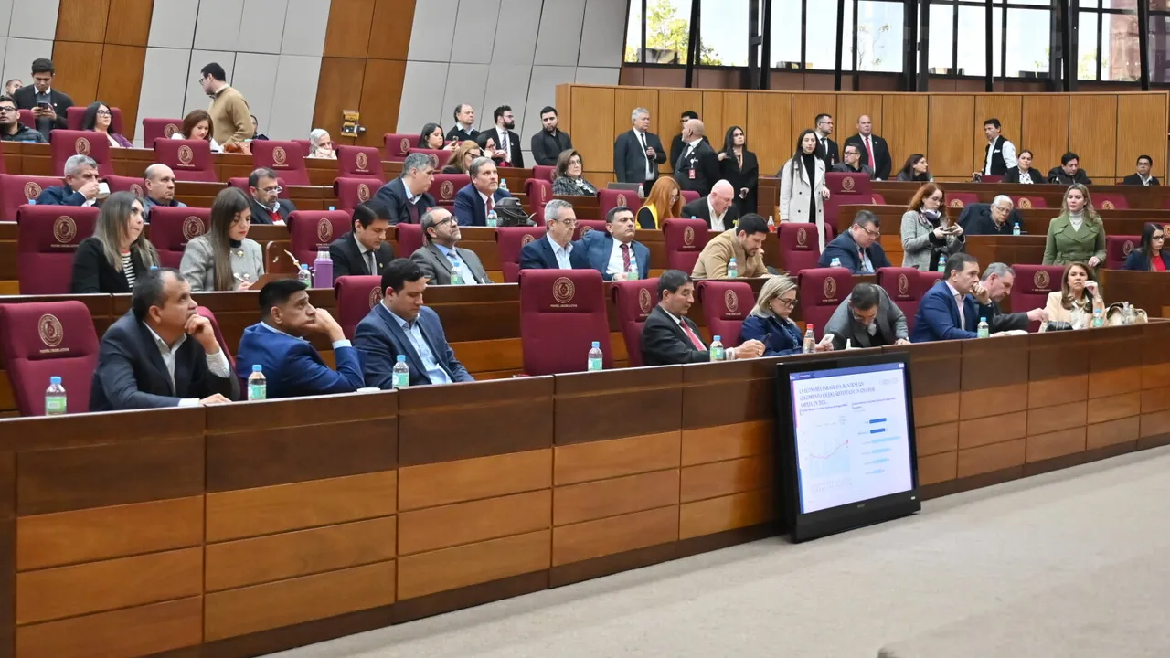 Legisladores paraguayos sentados en el Congreso durante una sesión, observando una pantalla con datos económicos.