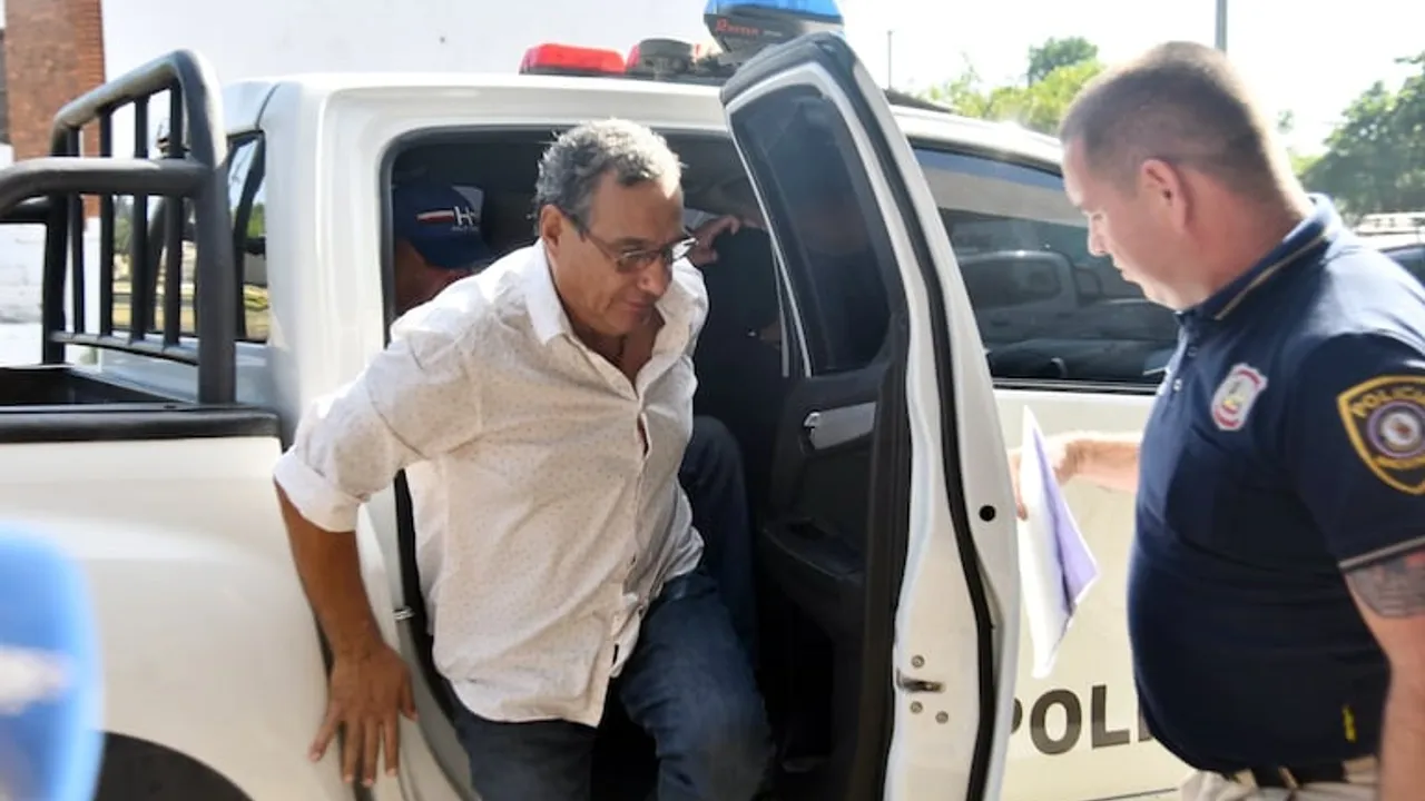 Hugo Javier González baja de una patrullera policial blanca asistido por un oficial de uniforme azul.