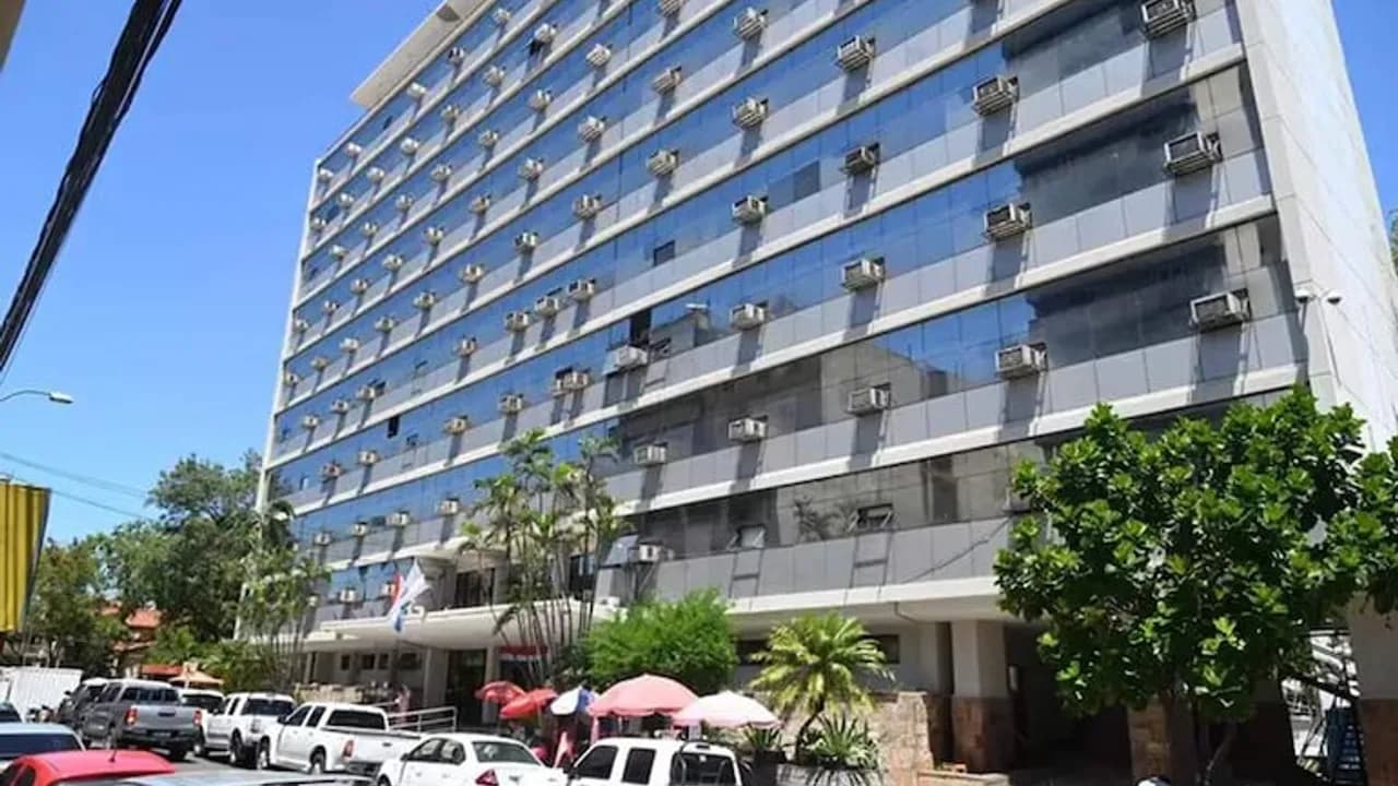 Fachada del edificio de vidrios azules del IPS con vehículos estacionados enfrente y árboles en la vereda.