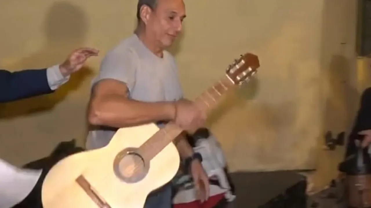 Hugo Javier González de pie sosteniendo una guitarra acústica de madera clara en un espacio interior.