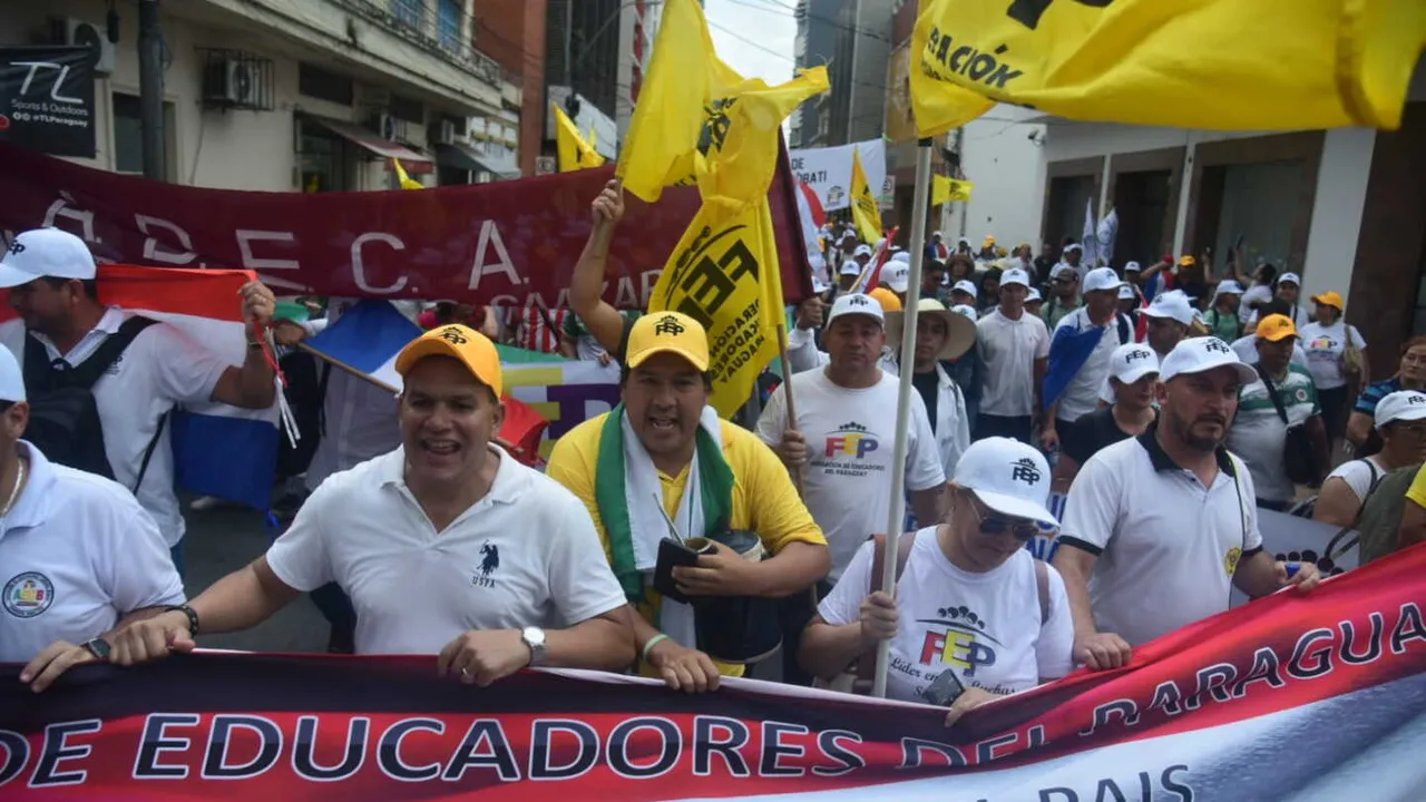 Manifestantes marchan sosteniendo banderas amarillas de la FEP y un cartel de educadores del Paraguay.