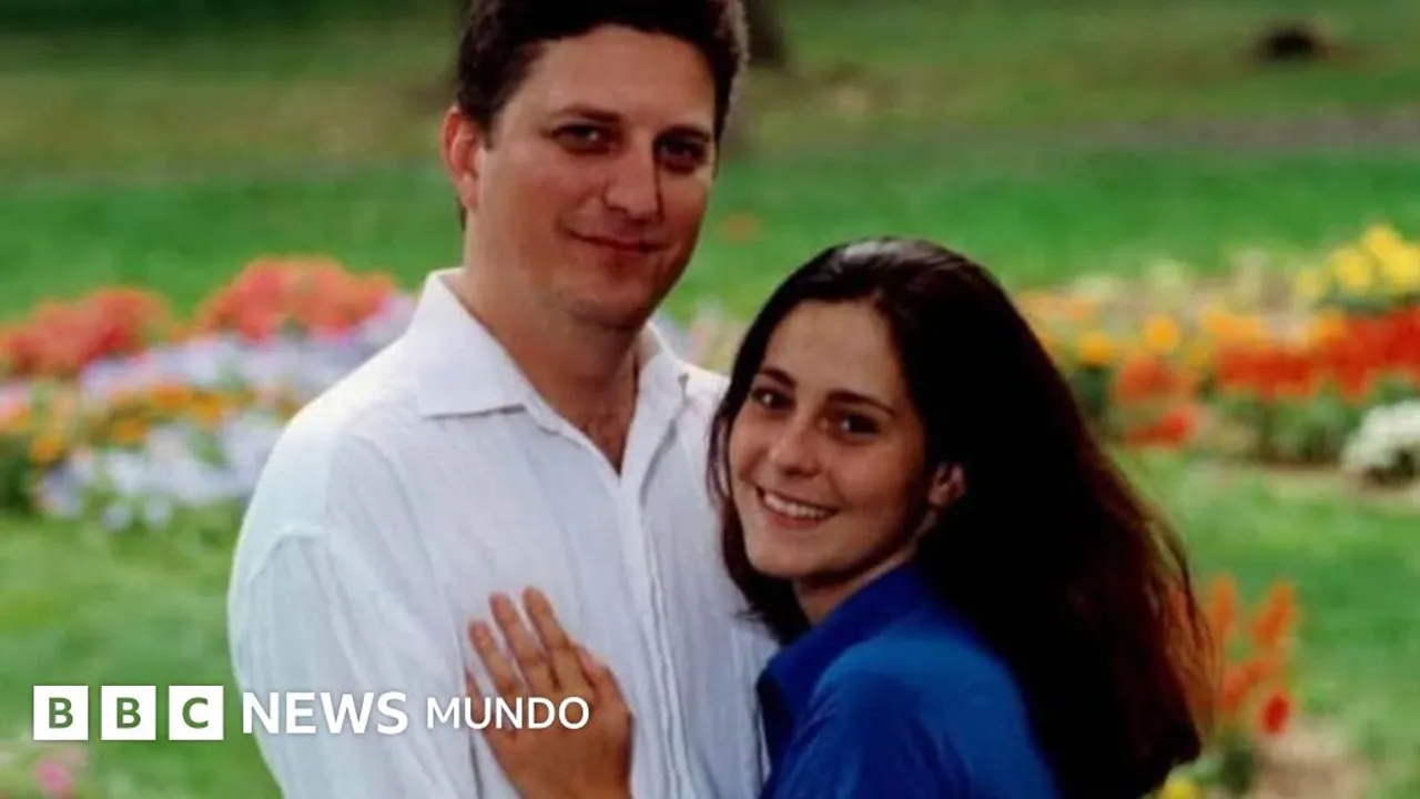 Un hombre con camisa blanca y una mujer con blusa azul sonríen abrazados en un jardín con flores.