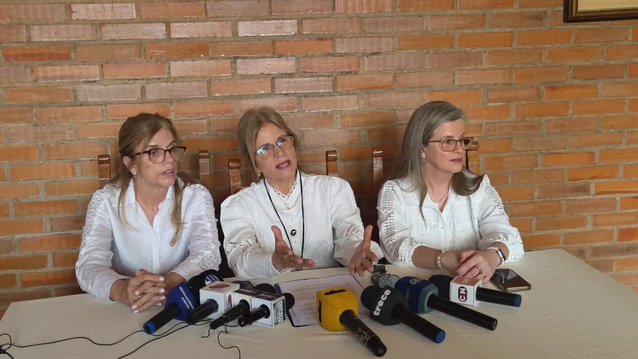 Beatriz, Silvana y Lorena Denis sentadas frente a varios micrófonos durante una conferencia de prensa ante una pared de ladrillos.