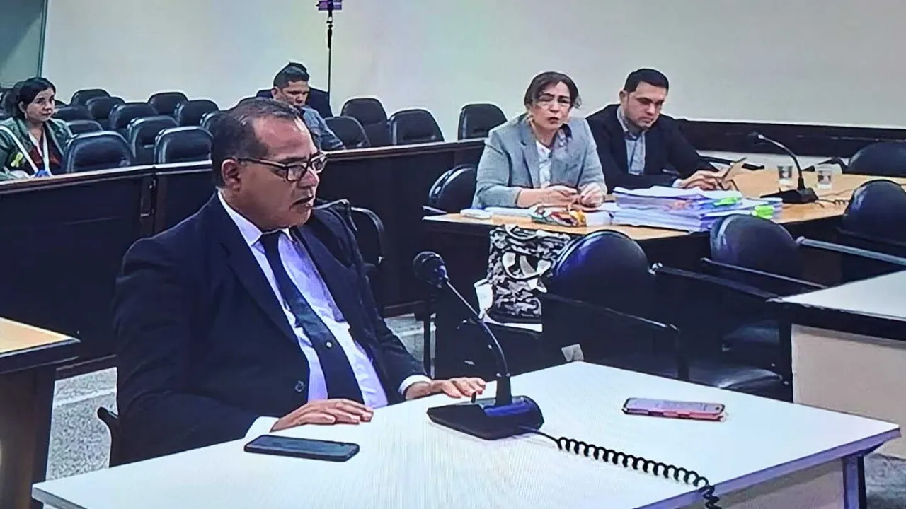 Un hombre de traje y anteojos declara ante un micrófono en una sala de juicio oral.