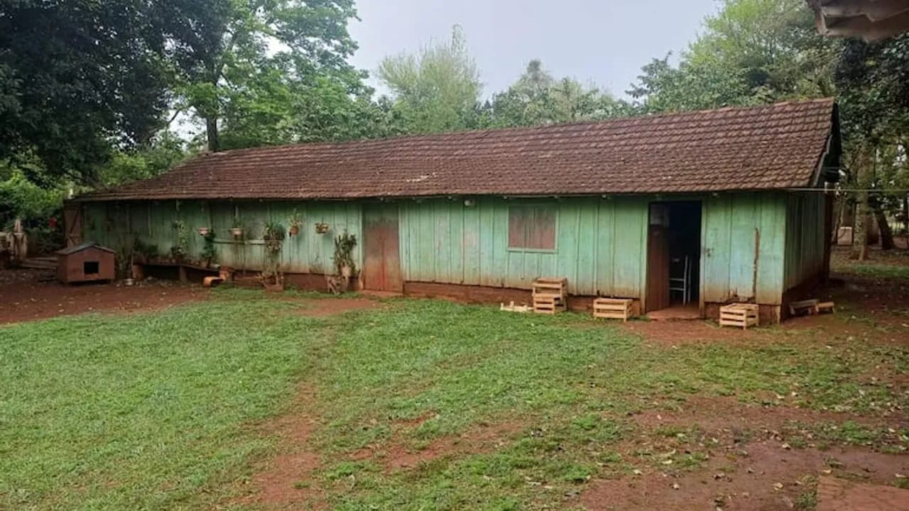 Antigua construcción alargada de madera verde con techo de tejas y un patio de pasto y tierra.