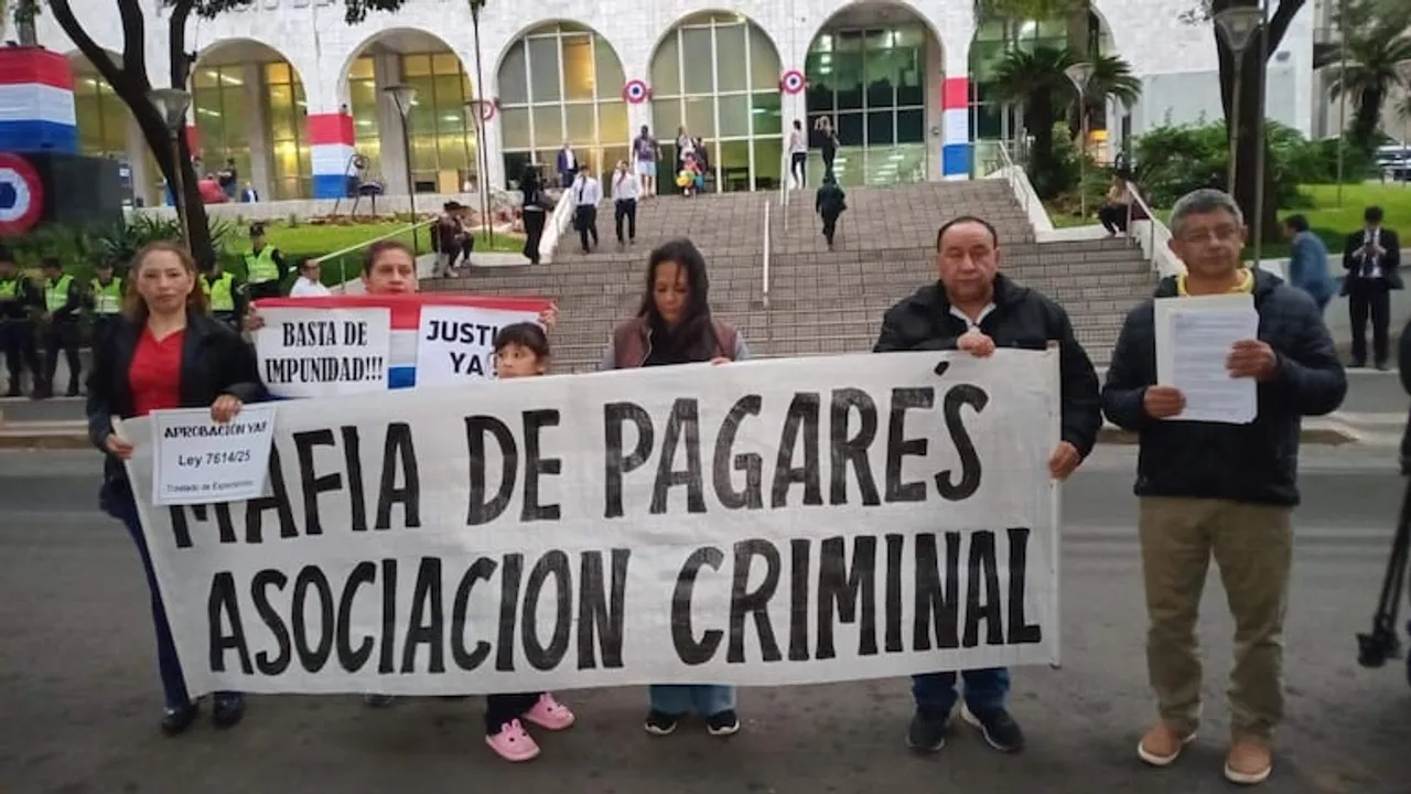 Cinco personas sostienen un cartel con la frase Mafia de pagarés asociación criminal frente a un edificio público.
