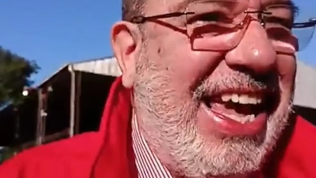Primer plano de Justo Zacarías Irún sonriendo con anteojos y una campera roja al aire libre.