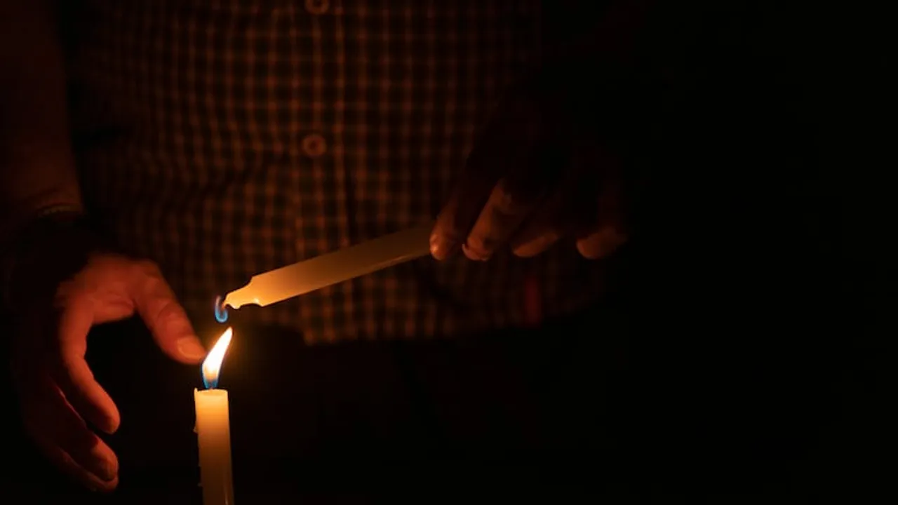 Manos sosteniendo una vela encendida para encender otra vela en medio de la oscuridad.