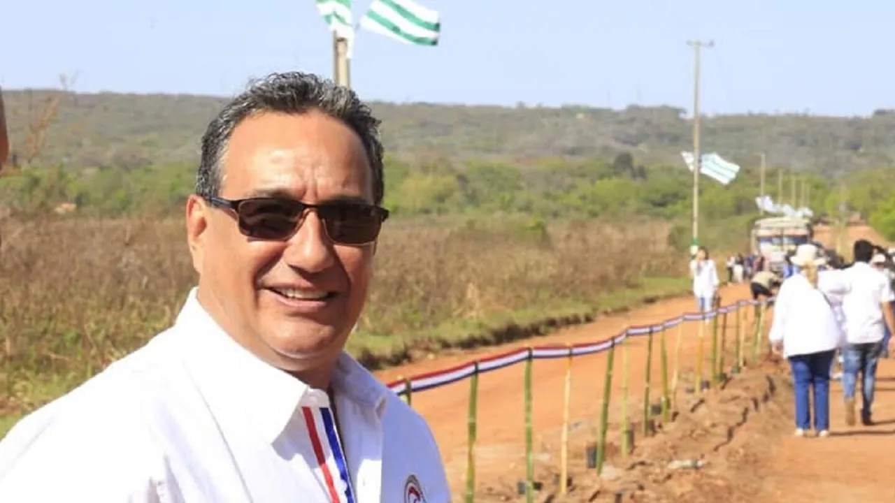 Hugo Javier González sonríe usando anteojos de sol y una camisa blanca, con un camino de tierra de fondo.
