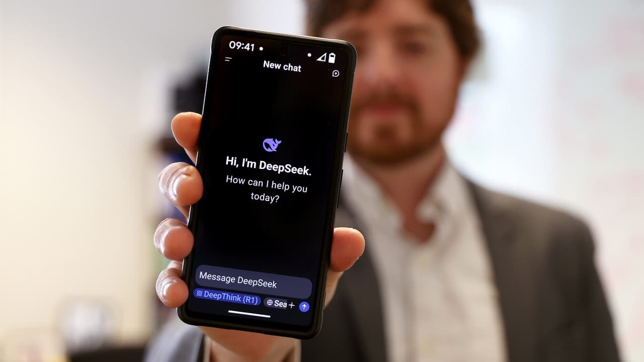 Mano sostiene un teléfono celular que muestra en pantalla la aplicación de chat de DeepSeek con fondo negro.
