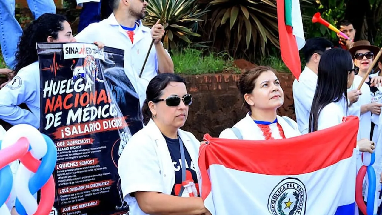 Medicos con batas blancas sostienen la bandera paraguaya y un cartel que exige un salario digno en una manifestacion.