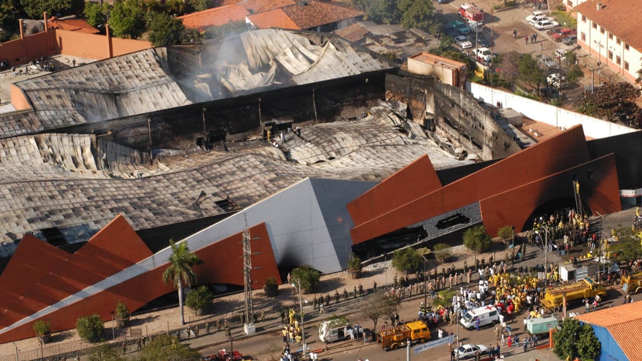 Vista aérea del supermercado Ycuá Bolaños destruido por el fuego, con el techo colapsado y vehículos de rescate afuera.