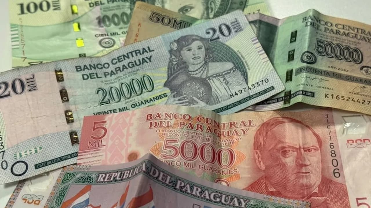Varios billetes de guaraníes paraguayos de diferentes denominaciones agrupados sobre una superficie clara.