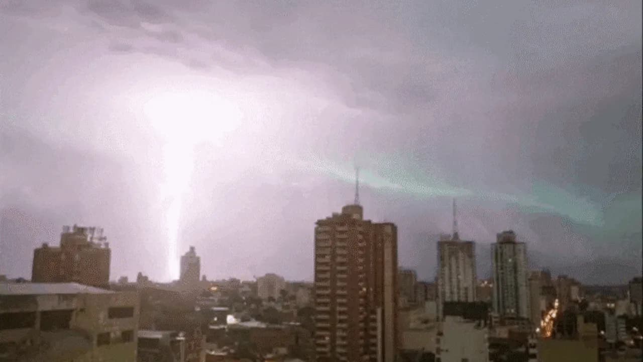 Un potente rayo ilumina el cielo nublado sobre los edificios de una ciudad durante una tormenta nocturna.