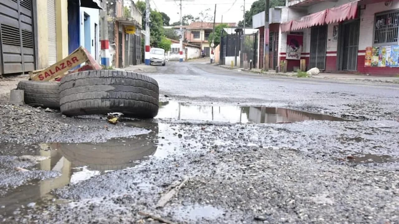 Neumáticos viejos y una caja de madera colocados sobre un gran bache con agua en una calle asfaltada de Asunción.