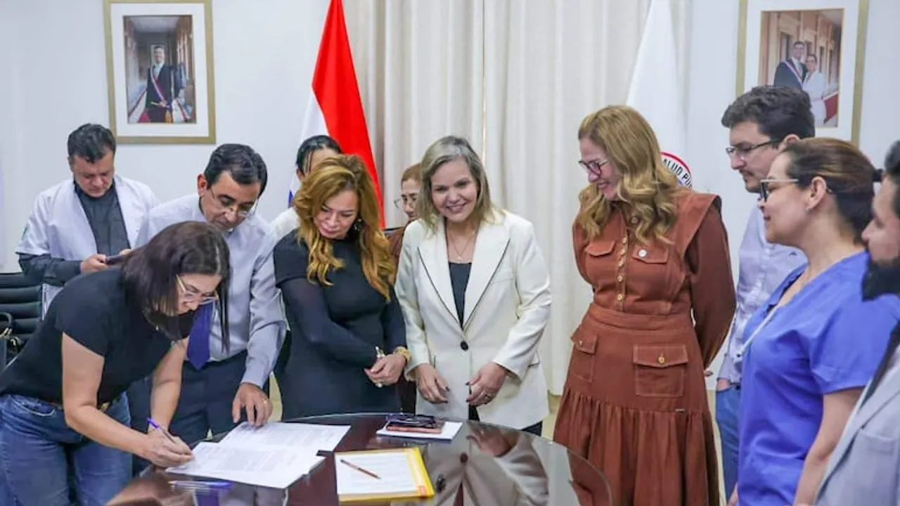 María Teresa Barán y Lilian Samaniego observan a una mujer firmando un acuerdo sobre una mesa redonda.