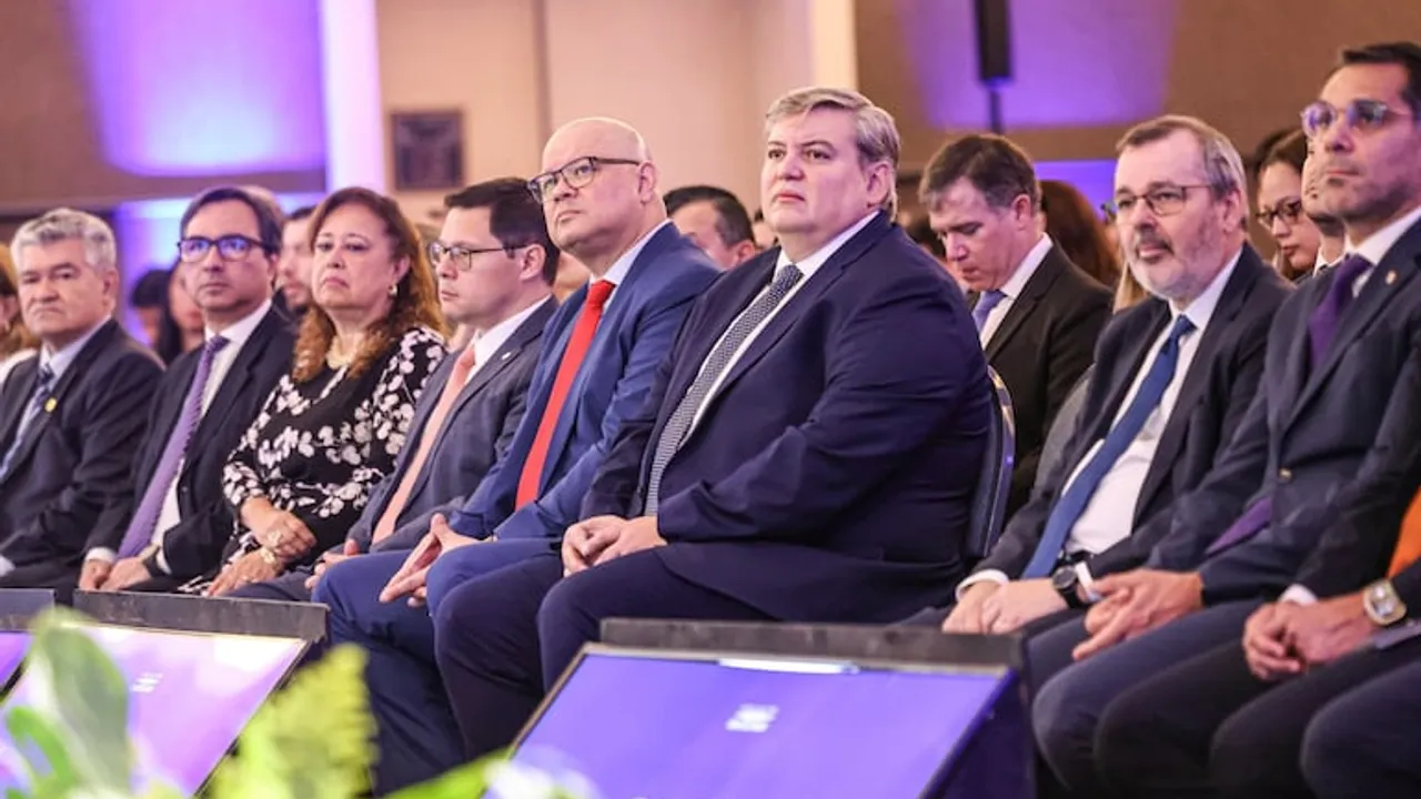 Hombres con trajes formales sentados en fila durante un evento oficial en un auditorio iluminado.
