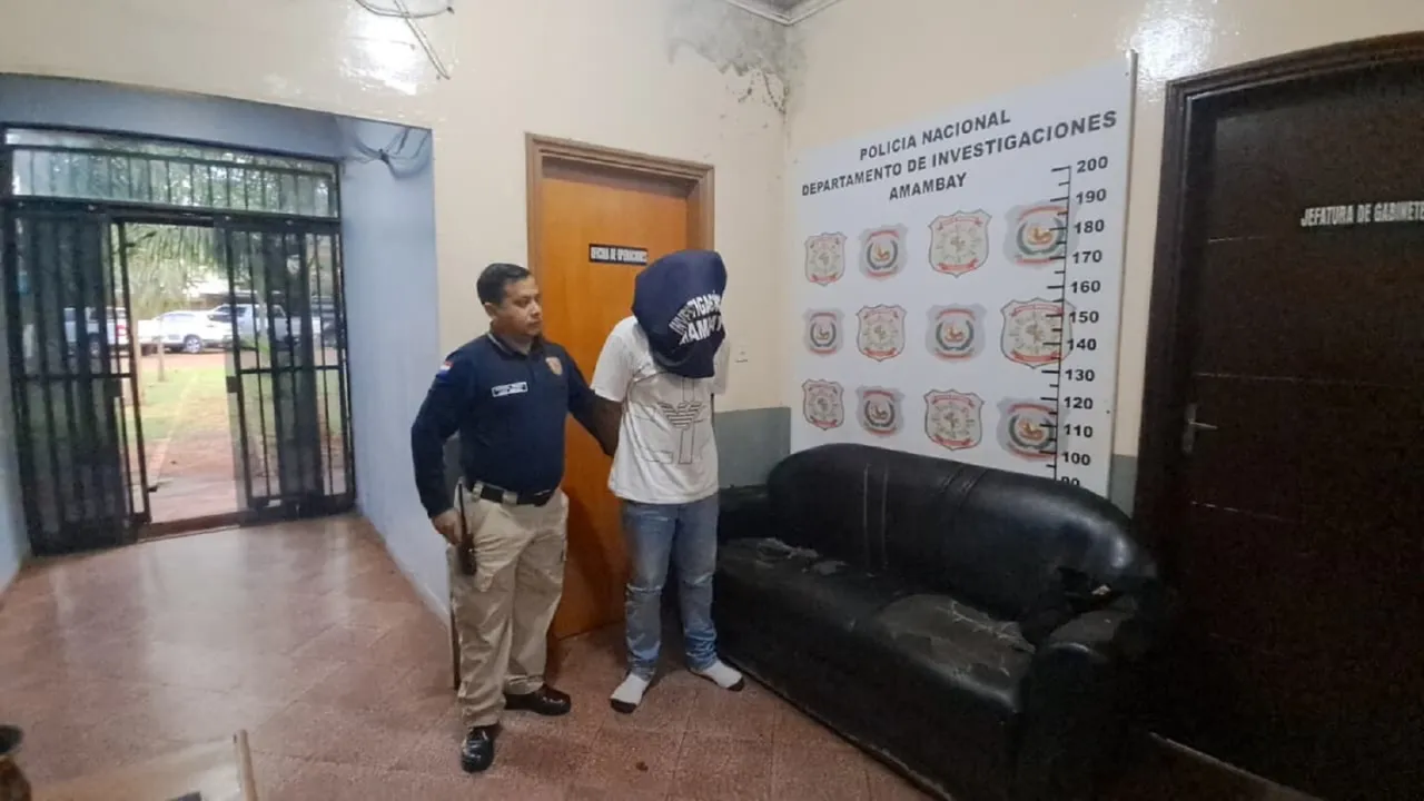 Un policía custodia a un detenido con la cabeza cubierta en la oficina de Investigaciones de Amambay.