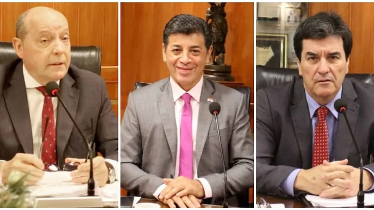 Tres hombres con traje y corbata sentados frente a micrófonos en una sala con paneles de madera.
