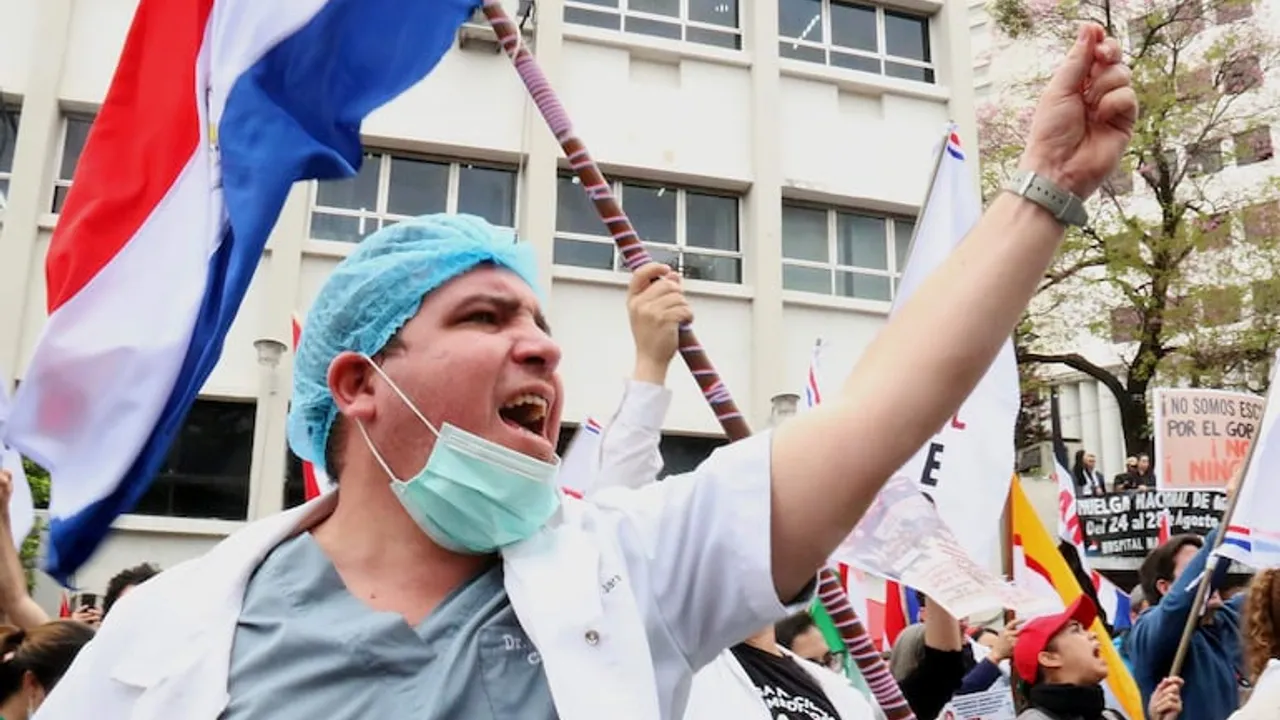 Médico con tapabocas y gorro quirúrgico grita sosteniendo la bandera de Paraguay durante una manifestación en la calle.