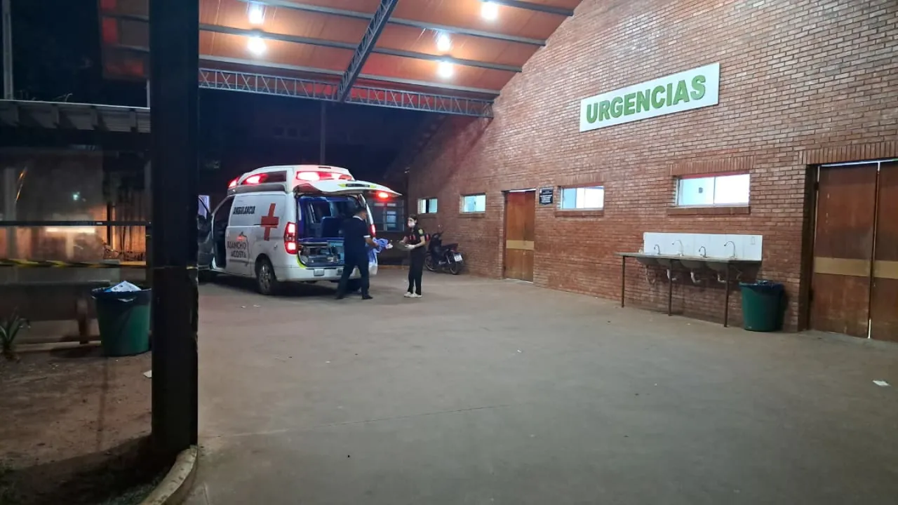 Ambulancia estacionada de noche frente al acceso de urgencias de un hospital con paredes de ladrillo visto.