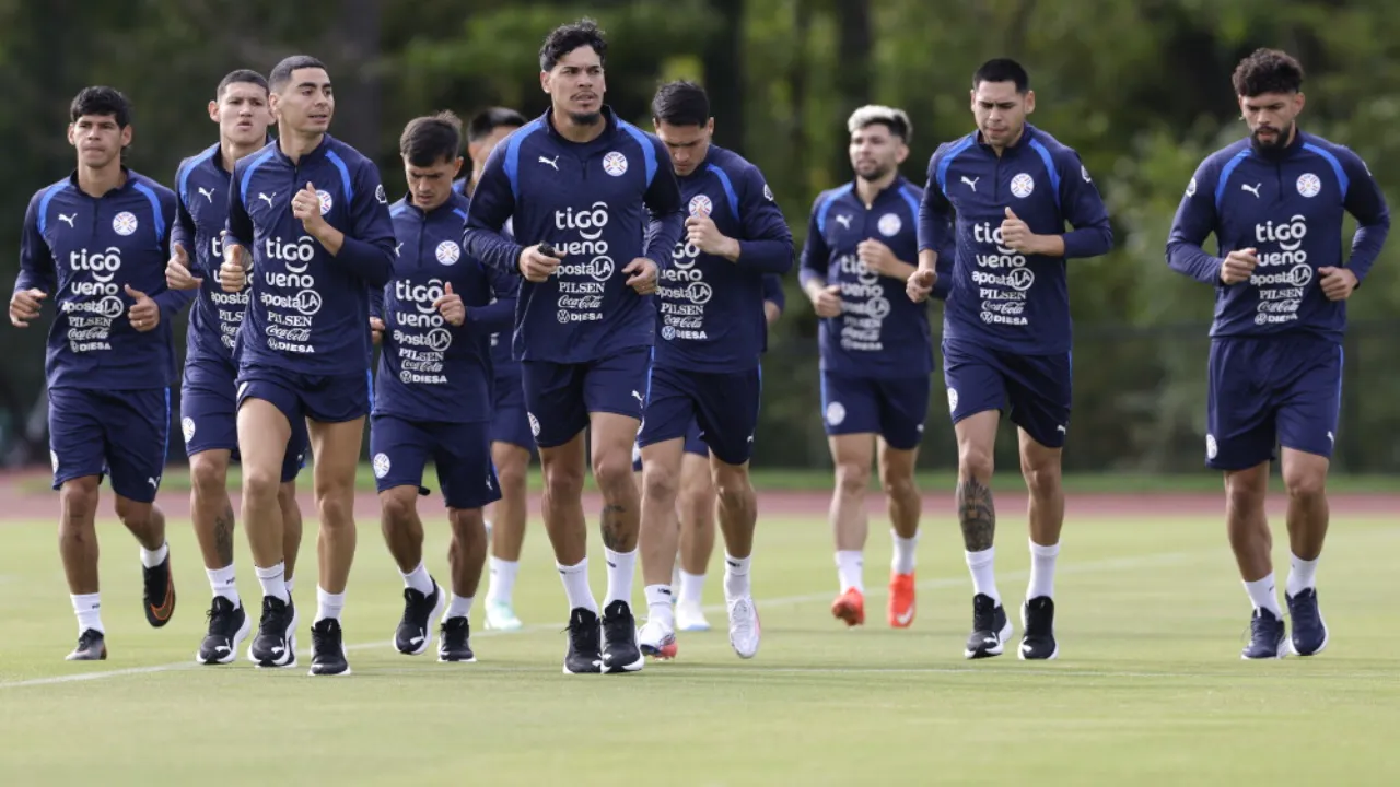 Futbolistas vestidos con indumentaria deportiva azul oscuro trotando sobre el césped durante un entrenamiento.