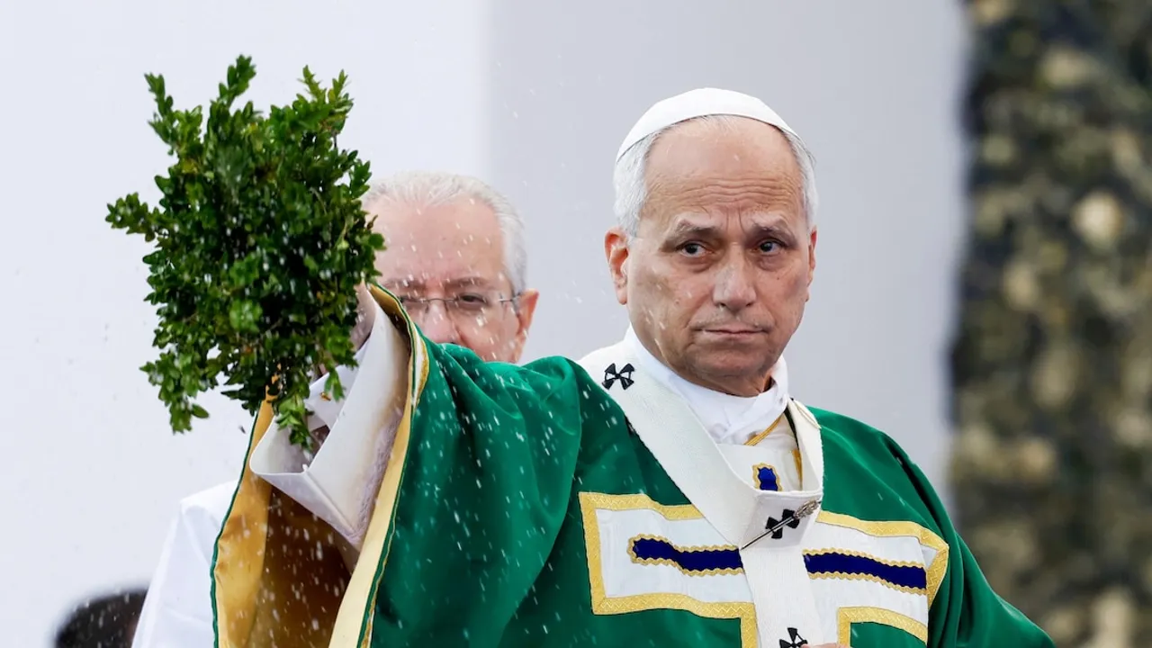 El papa León XIV con vestimenta verde bendice a los fieles con un ramo de hojas durante una misa al aire libre.
