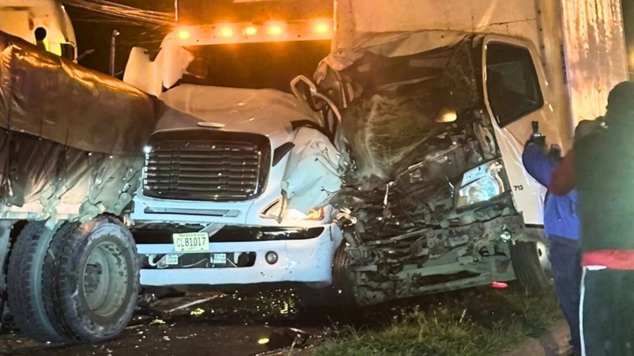 Camiones de carga y cabezales colisionados frontalmente con cabinas destrozadas sobre una carretera urbana iluminada