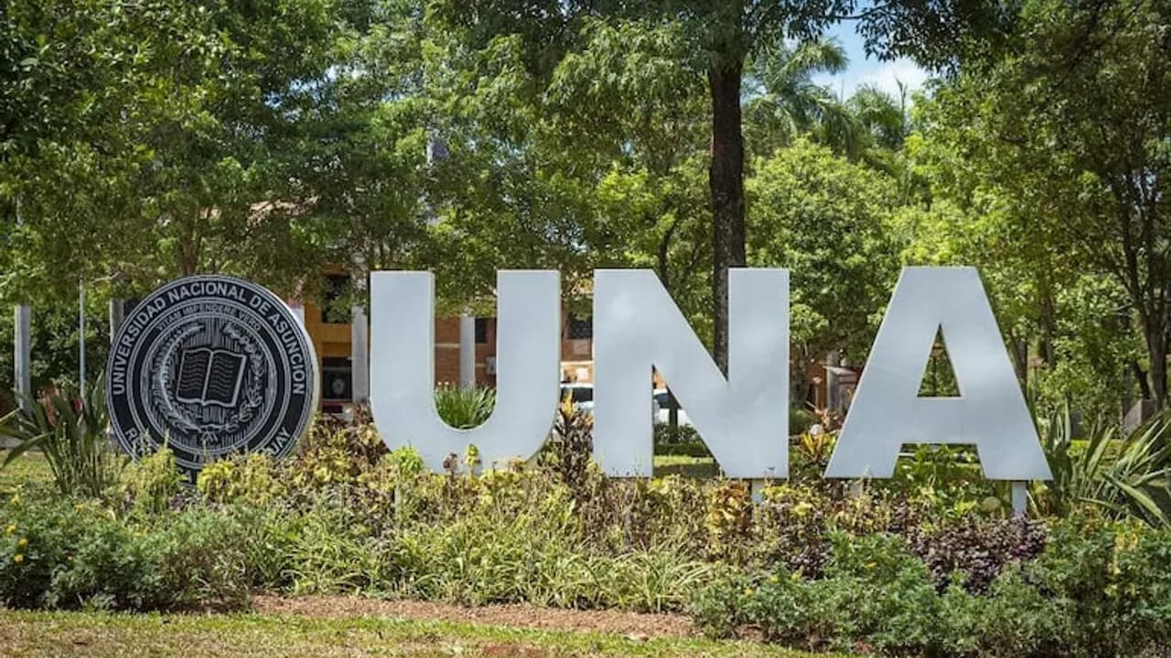 Cartel con las letras UNA y el escudo de la Universidad Nacional de Asunción rodeado de árboles y vegetación.