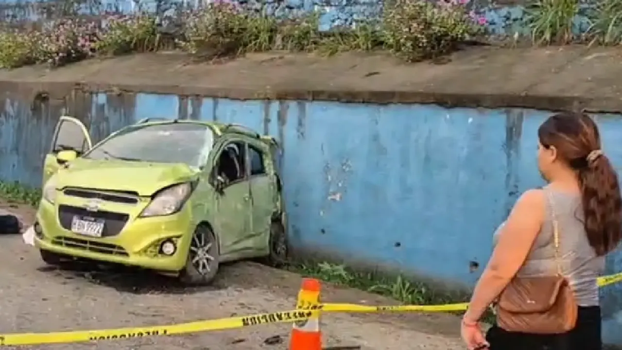 Automóvil verde chocado contra un muro azul al costado de una vía demarcada con cinta amarilla policial.