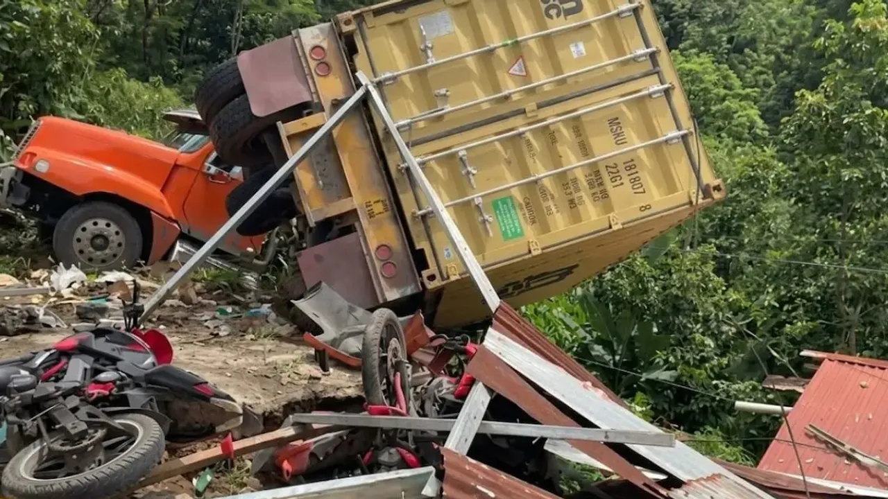 Camión de carga con contenedor volcado en un barranco sobre escombros y motocicletas destruidas al costado del camino