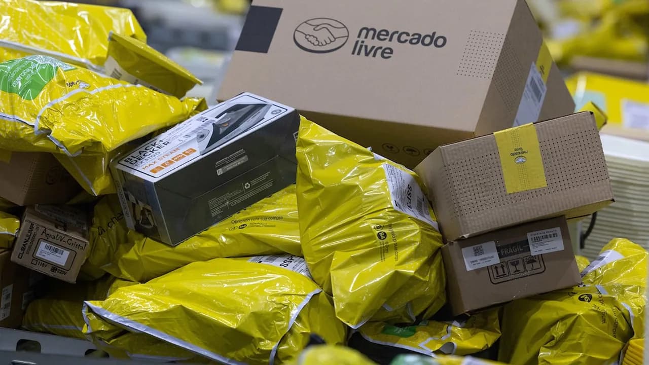 Paquetes amarillos y cajas de cartón con el logotipo de Mercado Libre apilados en un centro de distribución logística.