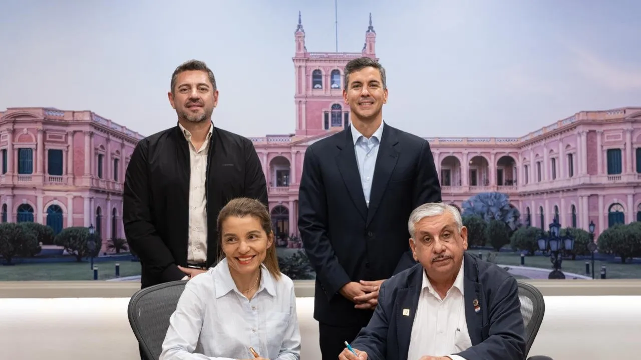 Autoridades gubernamentales y representantes gremiales firmando un acta frente a una imagen del Palacio de López.