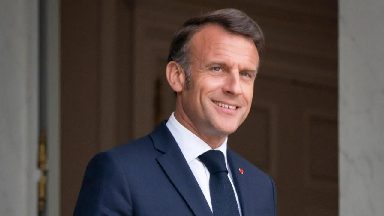 Emmanuel Macron sonríe vestido con traje azul oscuro y corbata durante un acto oficial en exteriores.