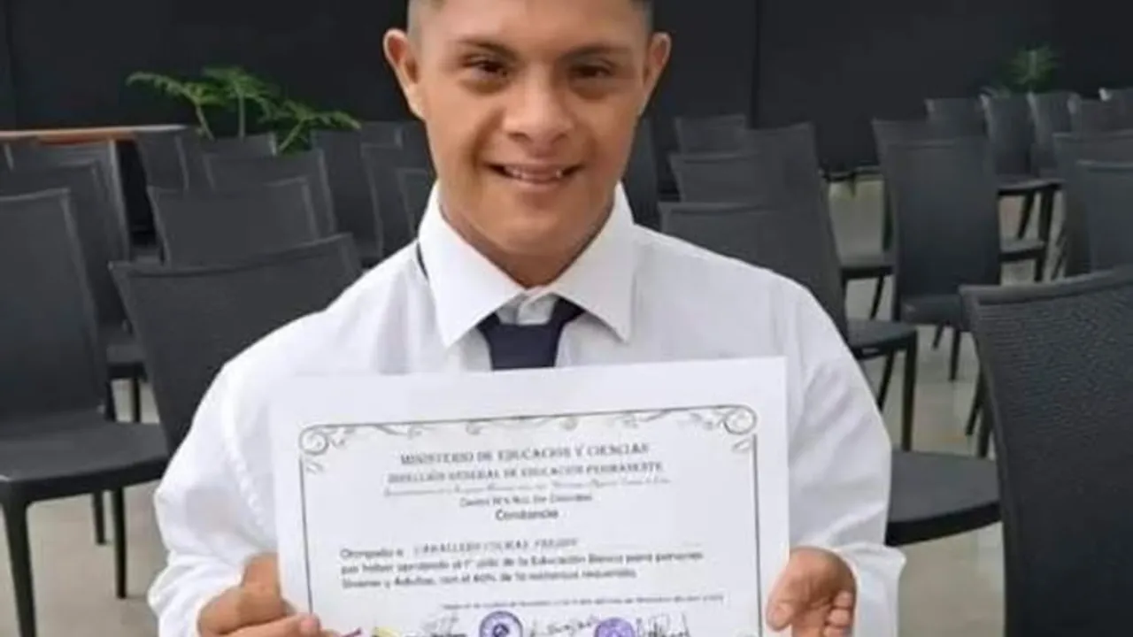 Freddy Caballero Colmán posa sonriente sosteniendo un certificado educativo oficial con camisa blanca y corbata.