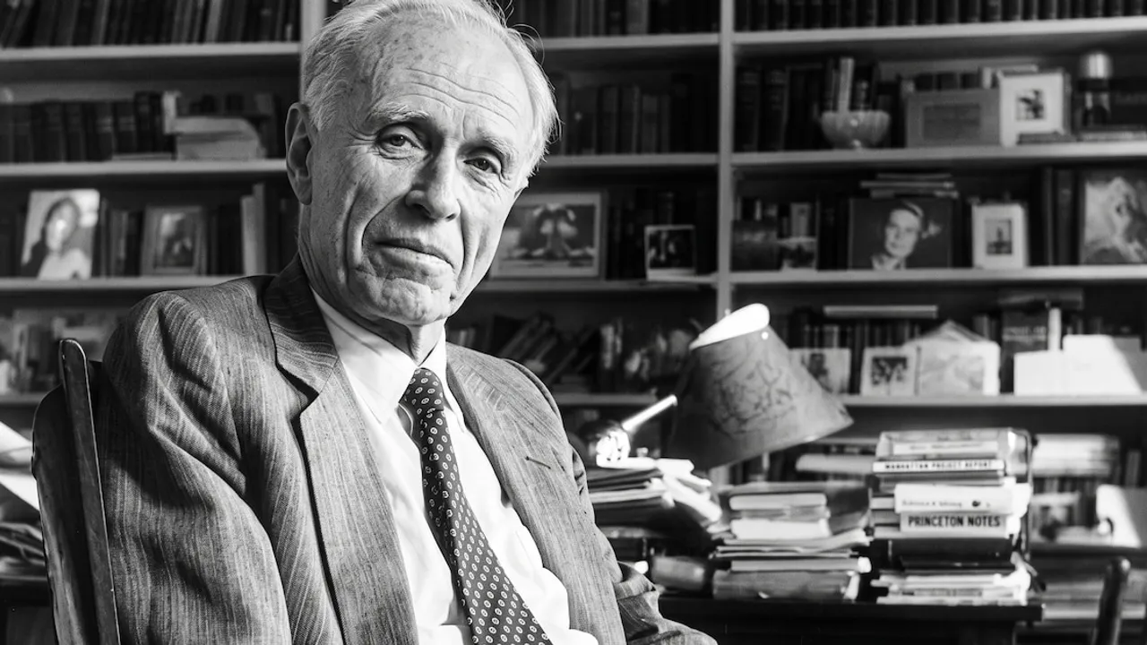 Adolfo Bioy Casares sentado en un sillón con traje y corbata frente a una gran biblioteca repleta de libros.