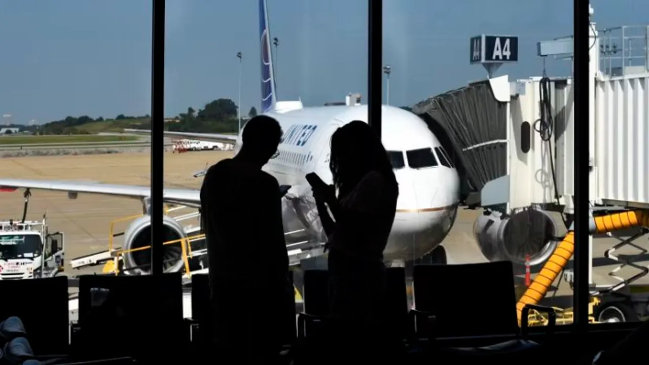 Siluetas de dos pasajeros frente a un ventanal que da a un avión en la pista de un aeropuerto.
