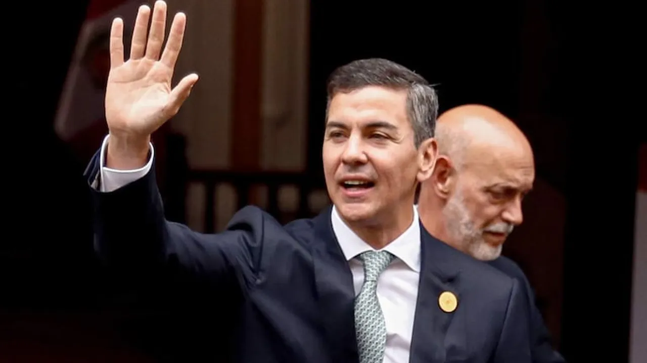Santiago Peña vestido con traje oscuro y corbata clara levantando la mano derecha en un saludo.
