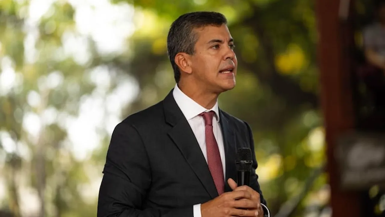 Santiago Peña vestido con traje oscuro y corbata habla sosteniendo un micrófono al aire libre.