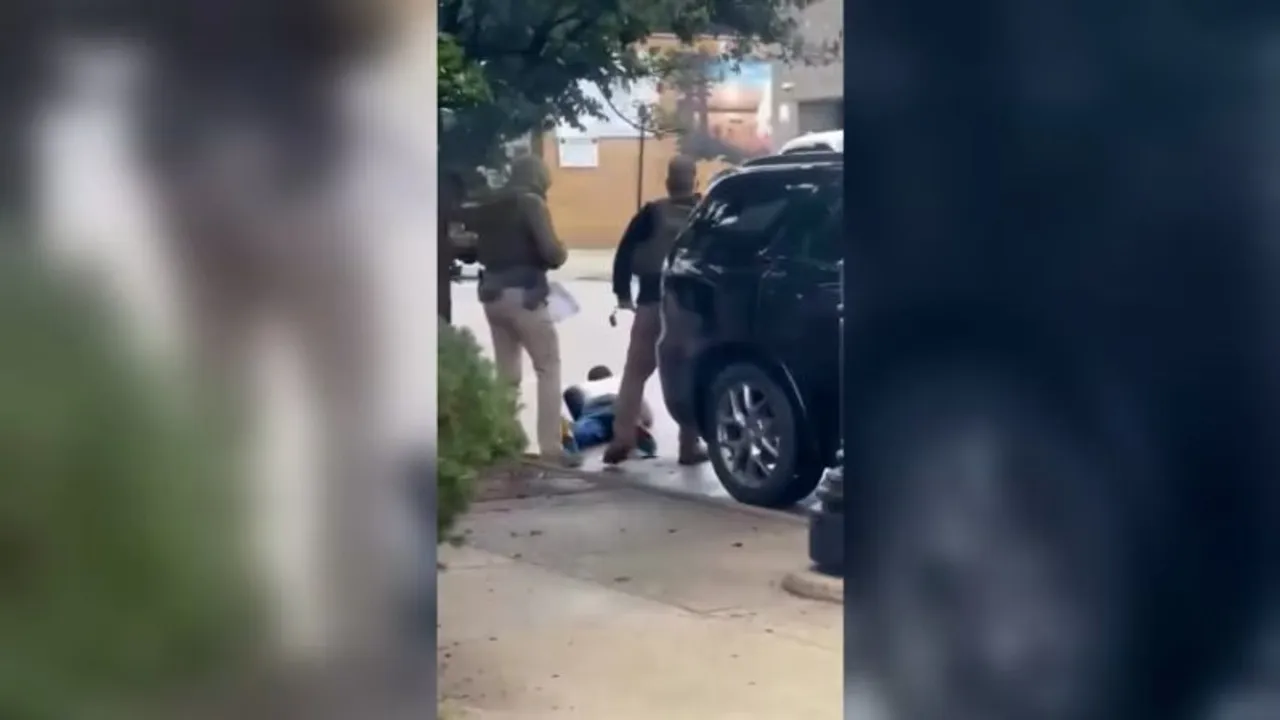 Dos agentes uniformados de espaldas junto a una camioneta mientras una persona permanece tendida en la acera.