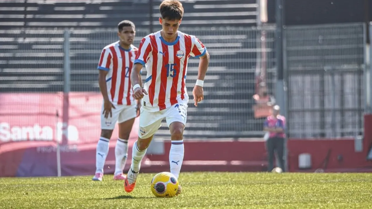Futbolista juvenil con camiseta albirroja conduce el balón sobre el césped durante un partido oficial
