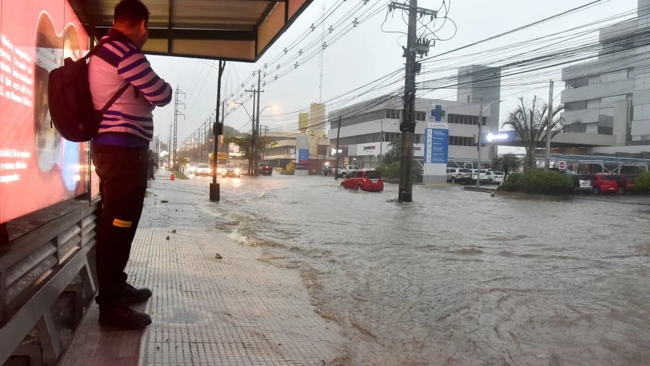 Un hombre espera el colectivo en una parada inundada por el raudal en una transitada avenida.