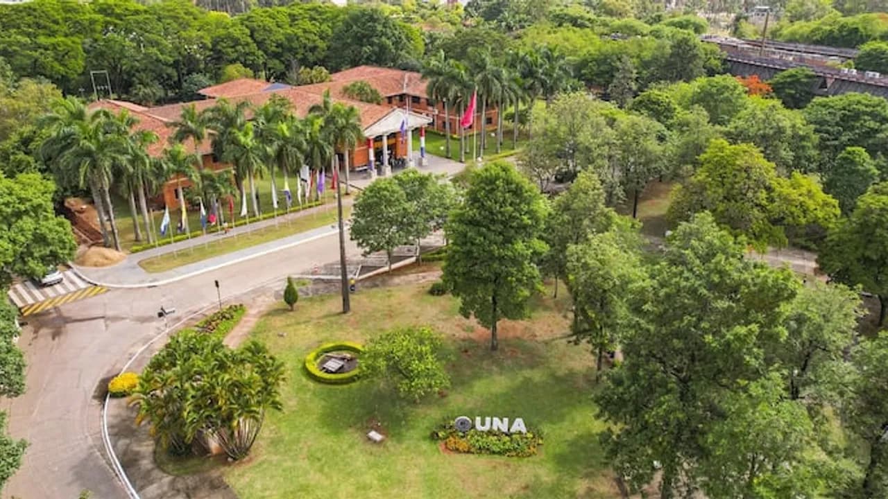 Vista aérea del campus universitario con jardines arbolados, caminos internos y el cartel distintivo de la institución.