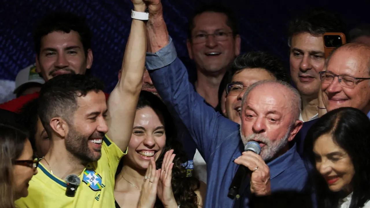Lula da Silva sostiene un micrófono y levanta la mano de André Janones en un escenario repleto de personas.