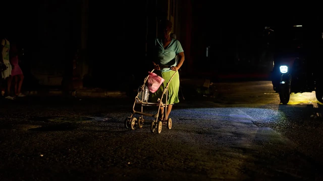 Persona empujando un cochecito de bebé cargado en una calle oscura iluminada por las luces de una motocicleta