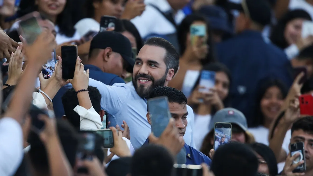 Nayib Bukele sonríe rodeado de una multitud de personas que intentan fotografiarlo con sus teléfonos móviles.
