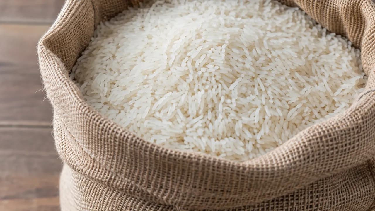 Bolsa de arpillera abierta y llena de granos de arroz blanco de grano largo sobre una mesa de madera.