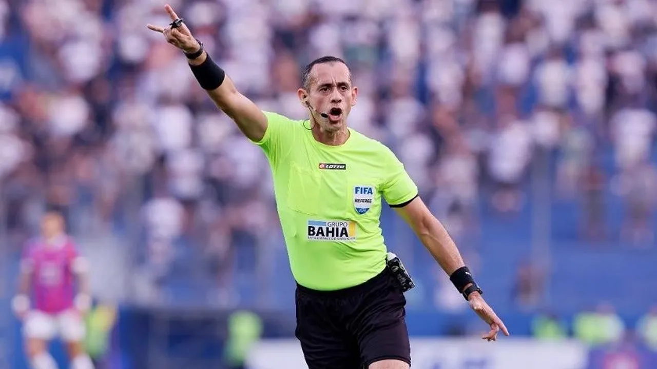 Árbitro de fútbol con remera verde flúor señalando con el brazo levantado durante un partido.