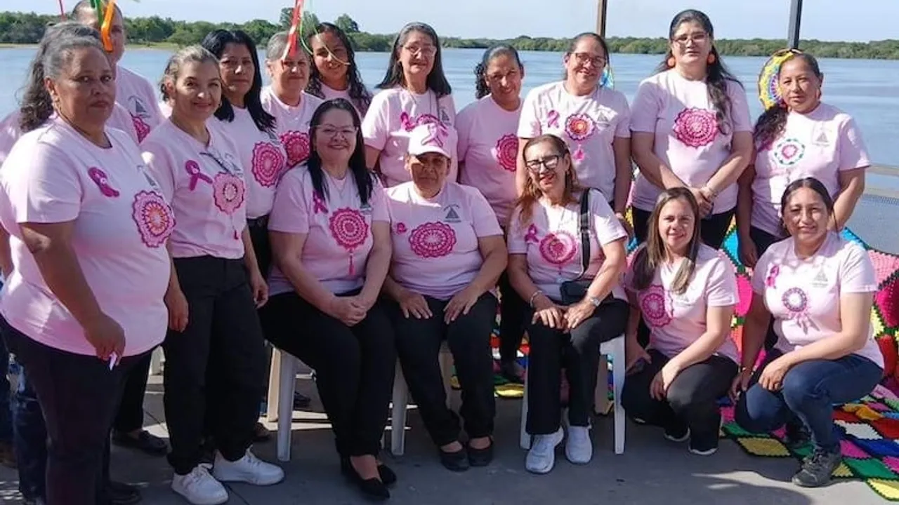 Grupo de mujeres con remeras rosadas posan sonrientes al aire libre cerca de la orilla de un río.