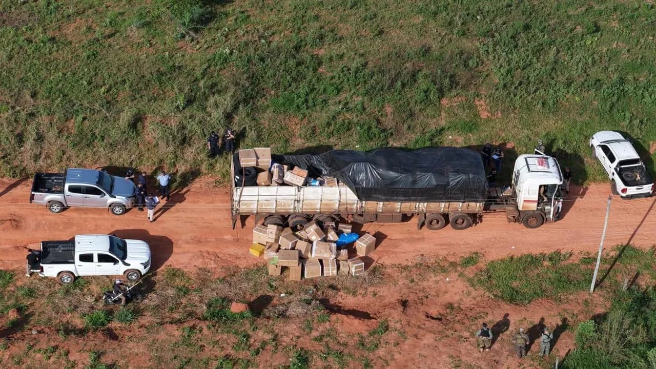 Camión de carga sobre camino de tierra con cajas esparcidas y agentes policiales inspeccionando la zona.